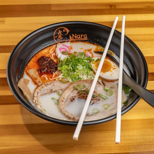 A bowl of Nara Sushi Ramen's spicy tonkotsu ramen with pork, egg, scallions, and narutomaki.