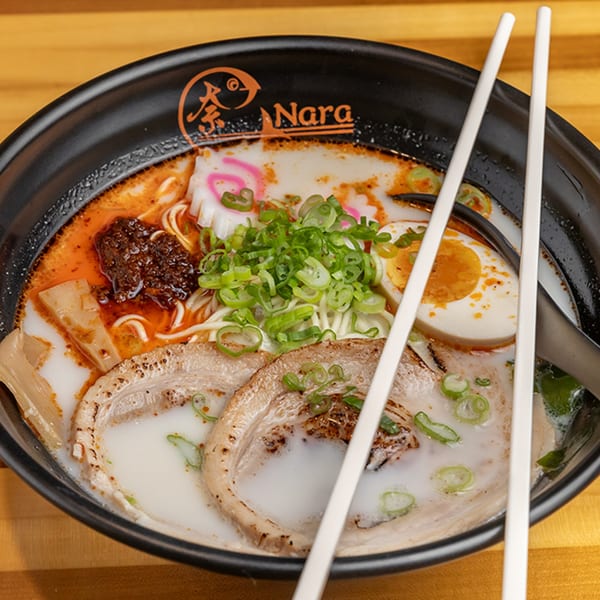 Nara Sushi Ramen's spicy tonkotsu ramen with pork, egg, scallions, and fish cake in a black bowl.