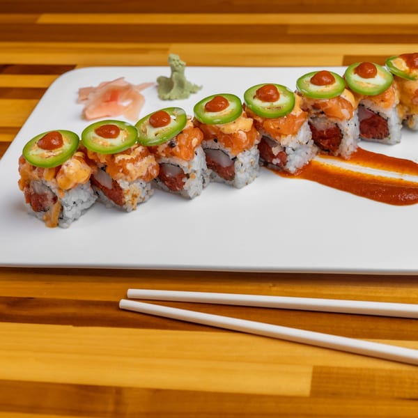 Spicy tuna sushi rolls topped with jalapeños and sauce, served with ginger, wasabi, and chopsticks.