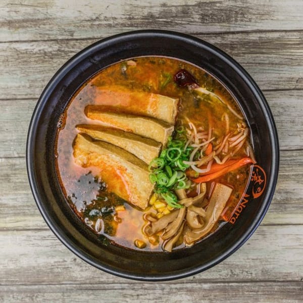 Overhead view of a Nara Sushi Ramen bowl with tofu, vegetables, and broth on a wooden table.